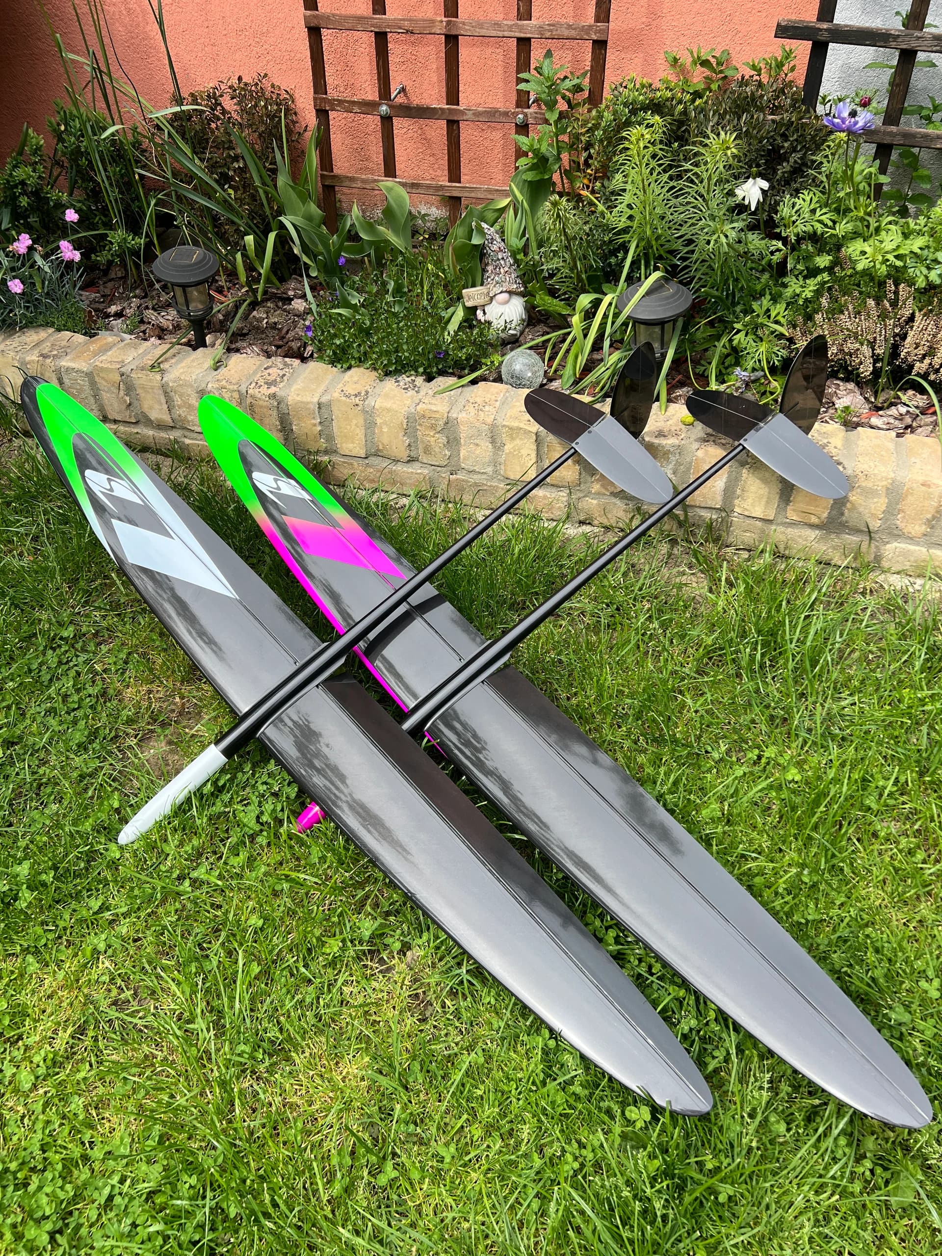 Two green and pink D1S gliders resting beside a garden wall