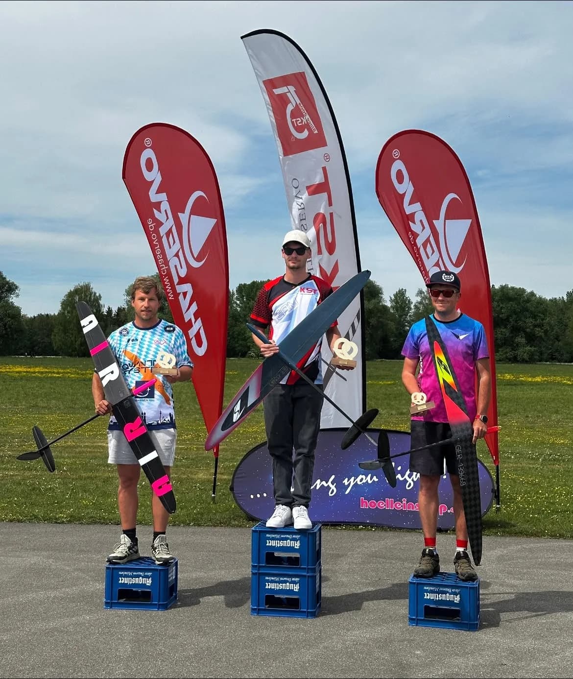 Three pilots with gliders on a competition podium beside FlyPeak flags
